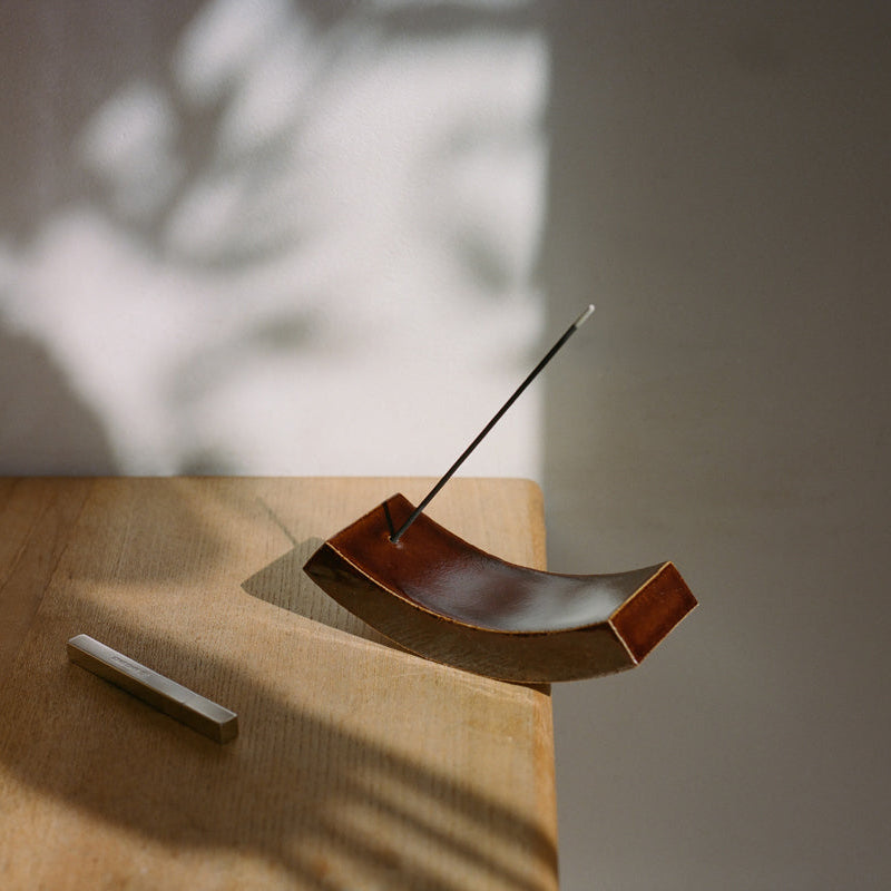 Wooden incense holder with a single incense stick on a wooden surface with a blurred background