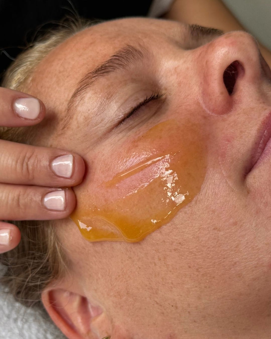 Close-up of a person applying a honey manuka mask to their face.