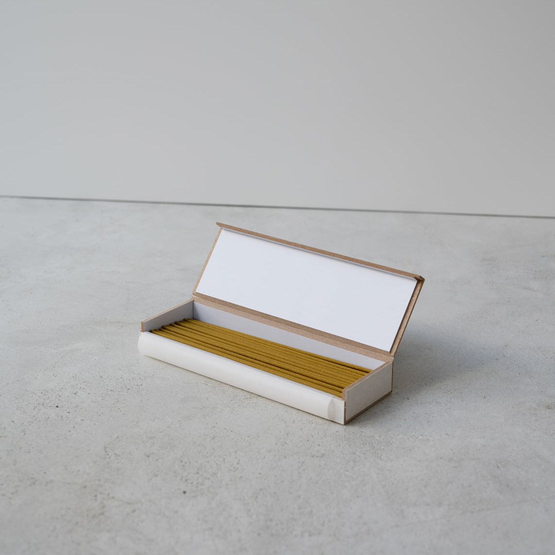 Open white box with yellow incense sticks on a gray surface