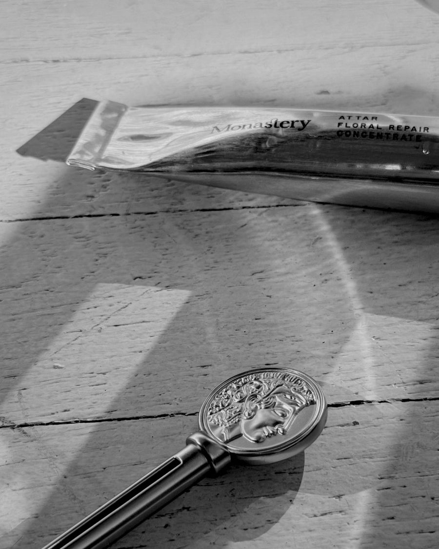 Decorative key with emblem on a wooden surface with silver tube of Monastery's Attar. Black and white image. 
