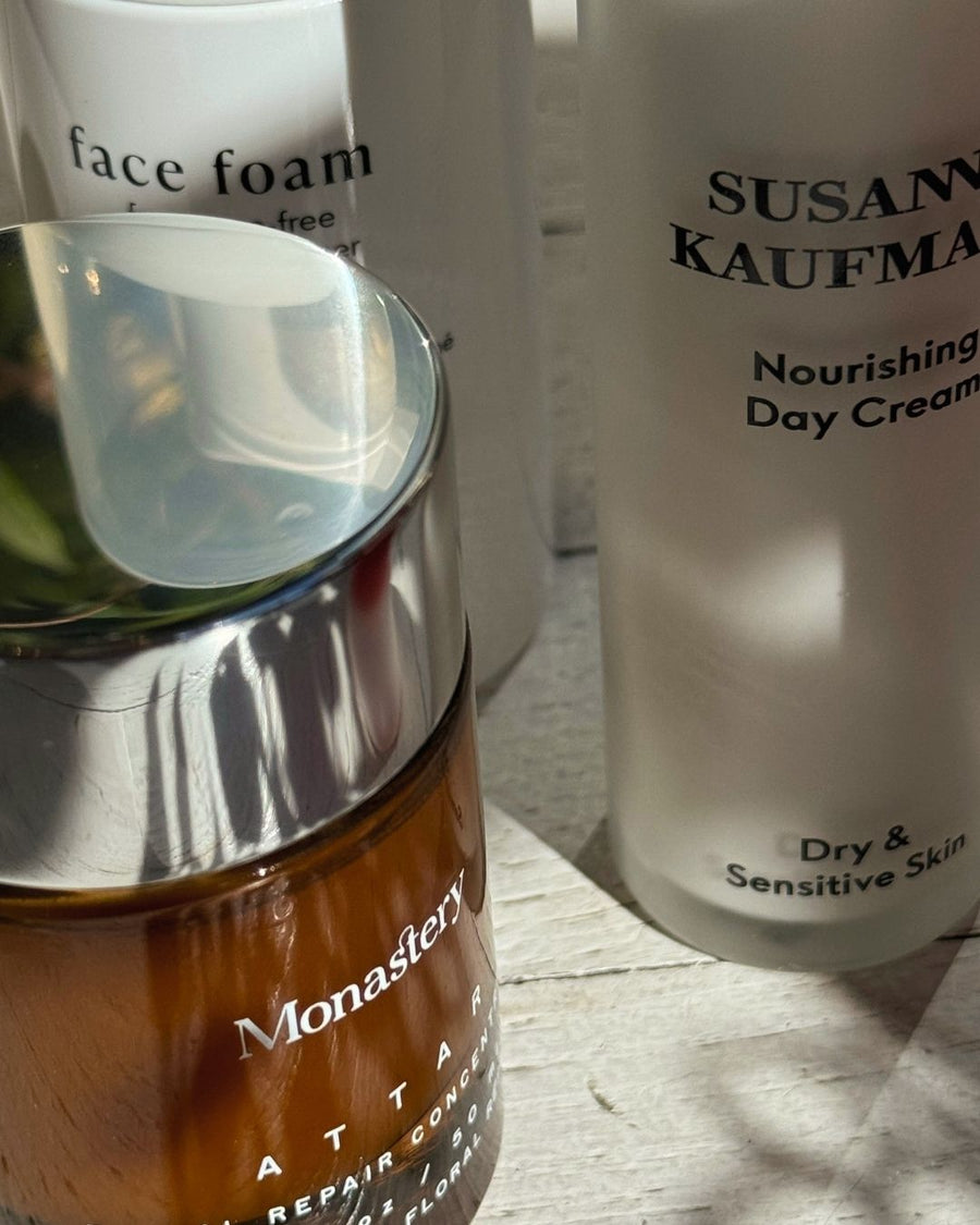 Skincare products including a brown jar of Monastery Attar and white bottles on a wooden surface.