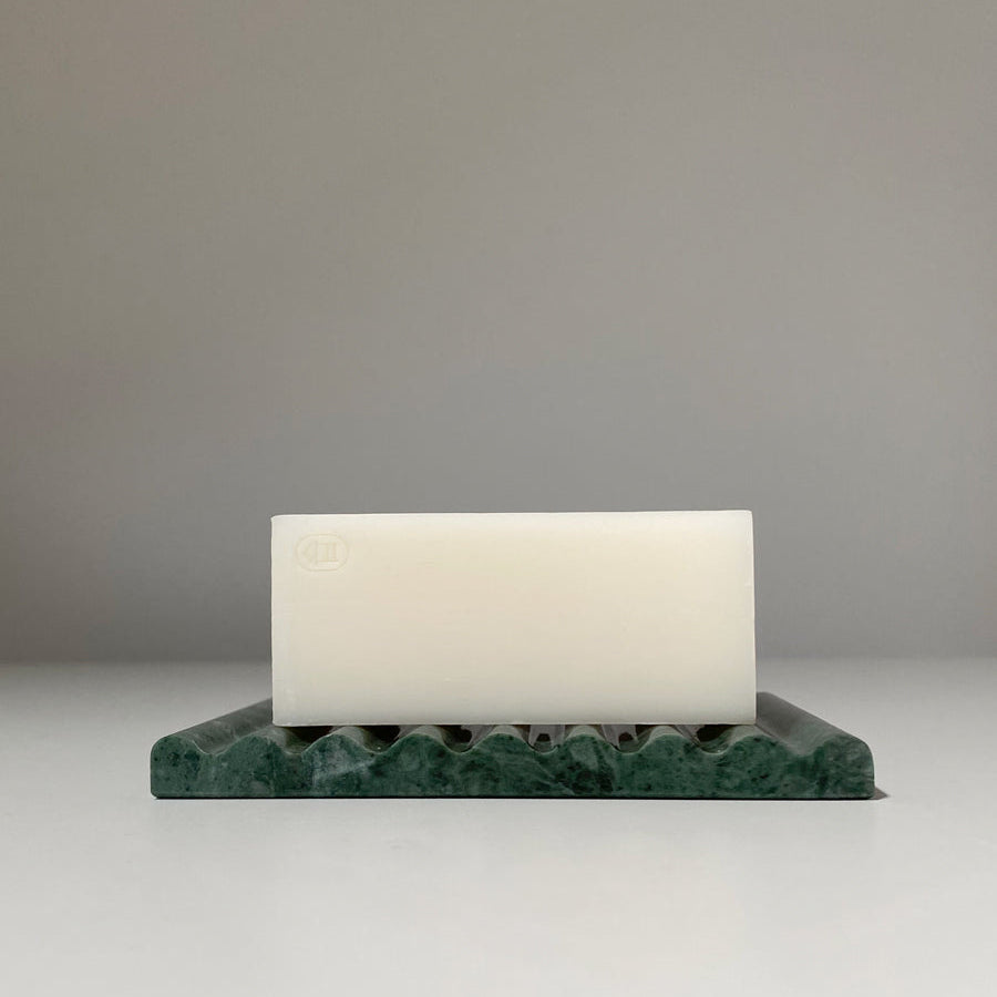 Rectangular white bar of soap on a green marble soap dish against a plain background